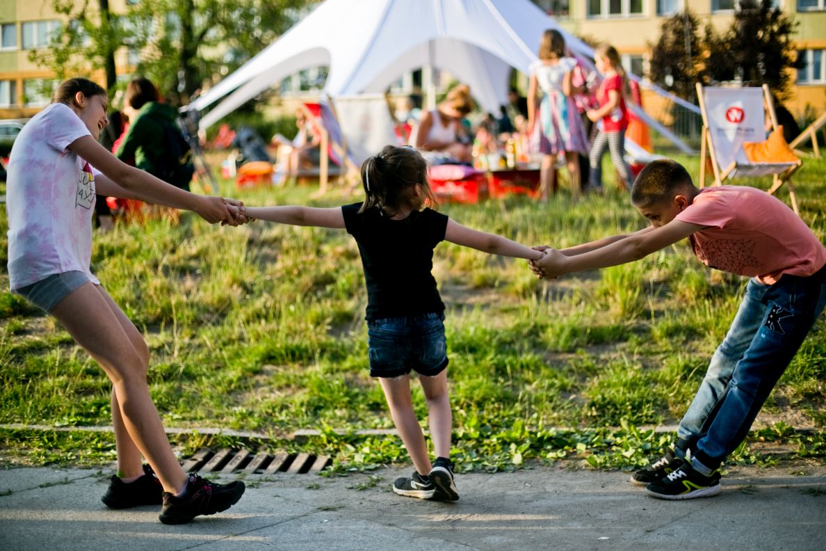 Dzieci trzymają za ręce dziewczynkę podczas zabawy. 