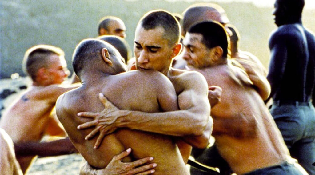 Zdjęcie przedstawia mężczyzn bez koszulek. Przedstawioną sytuację można odebrać wieloznacznie - zarówno jako przytulanie się, jak i jako walkę.