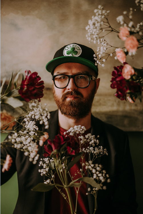 Mężczyzna noszący okulary w czapce z daszkiem i z kwiatami.